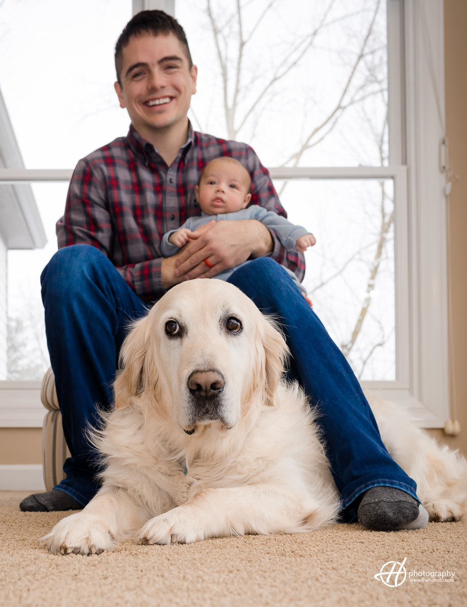 This image shows the bond between Tyler, his baby, and a loyal dog named Ace. Tyler is seen holding the baby, while Ace sits at his feet, watching over the family with devotion. The focus of the image is on Ace, who appears to be a constant presence of love and protection.