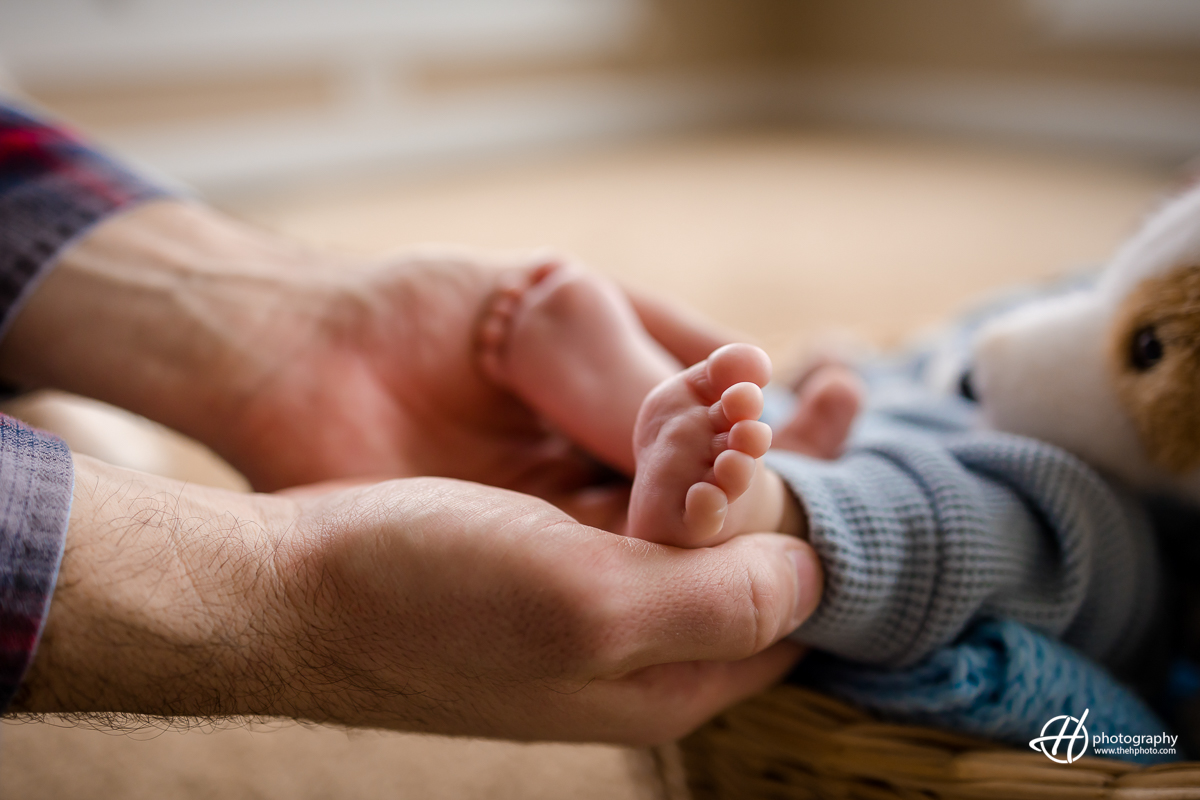 father is seen holding his newborn baby's feet in his hands. The image conveys a sense of intimacy and love, with the father's hands delicately cradling the baby's small feet.