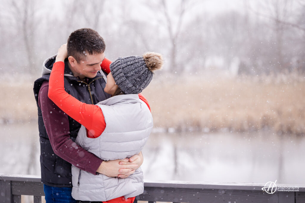 Alison and Tyler are seen sharing a kiss outside while snowflakes swirl around them. The photo captures the beauty and magic of winter, as well as the couple's love for each other. The image conveys a sense of warmth and happines