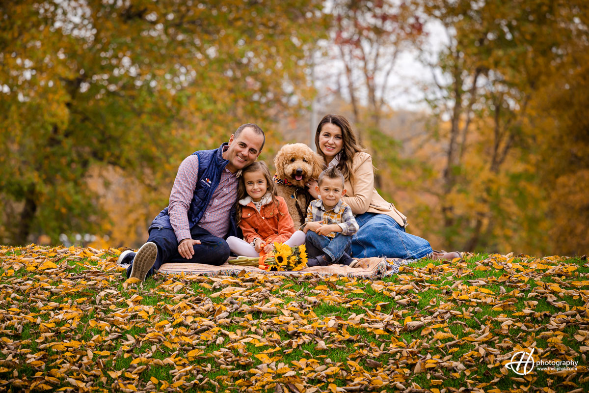Witness the Proca family, decked in cozy fall attire, surrounded by the warm hues of autumn leaves. Denver, their energetic canine companion, joyfully joins the family huddle, creating a picture-perfect moment of unity amidst nature's seasonal spectacle.