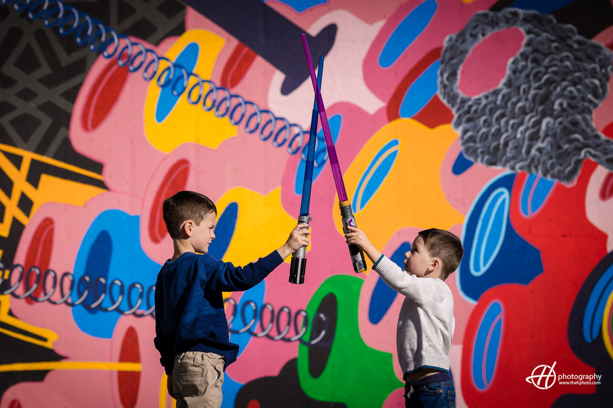 Dorian and Theo unleash their inner Star Wars heroes against a backdrop of vibrant wall paintings in Elgin. With imaginary lightsabers in hand, the siblings immerse themselves in an epic galactic adventure, their expressions a mix of excitement and joy. The colorful artwork adds a whimsical touch to this playful moment, blending creativity and childhood wonder.