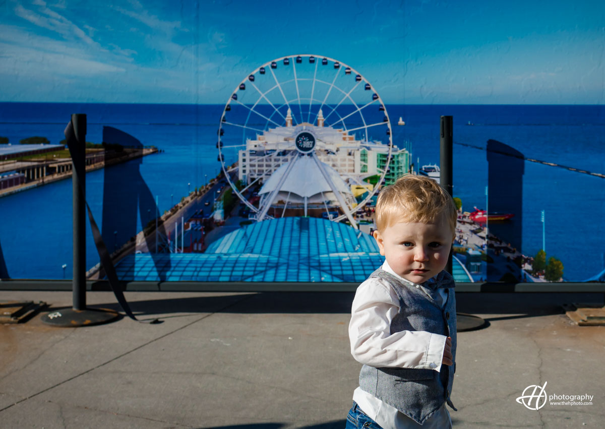 Cherished family moment: A heartwarming scene unfolds as Sara and Todd cradle their adorable baby against the stunning backdrop of Navy Pier. The Chicago skyline, framed by the iconic Navy Pier arch, adds a touch of urban charm to this precious family portrait.