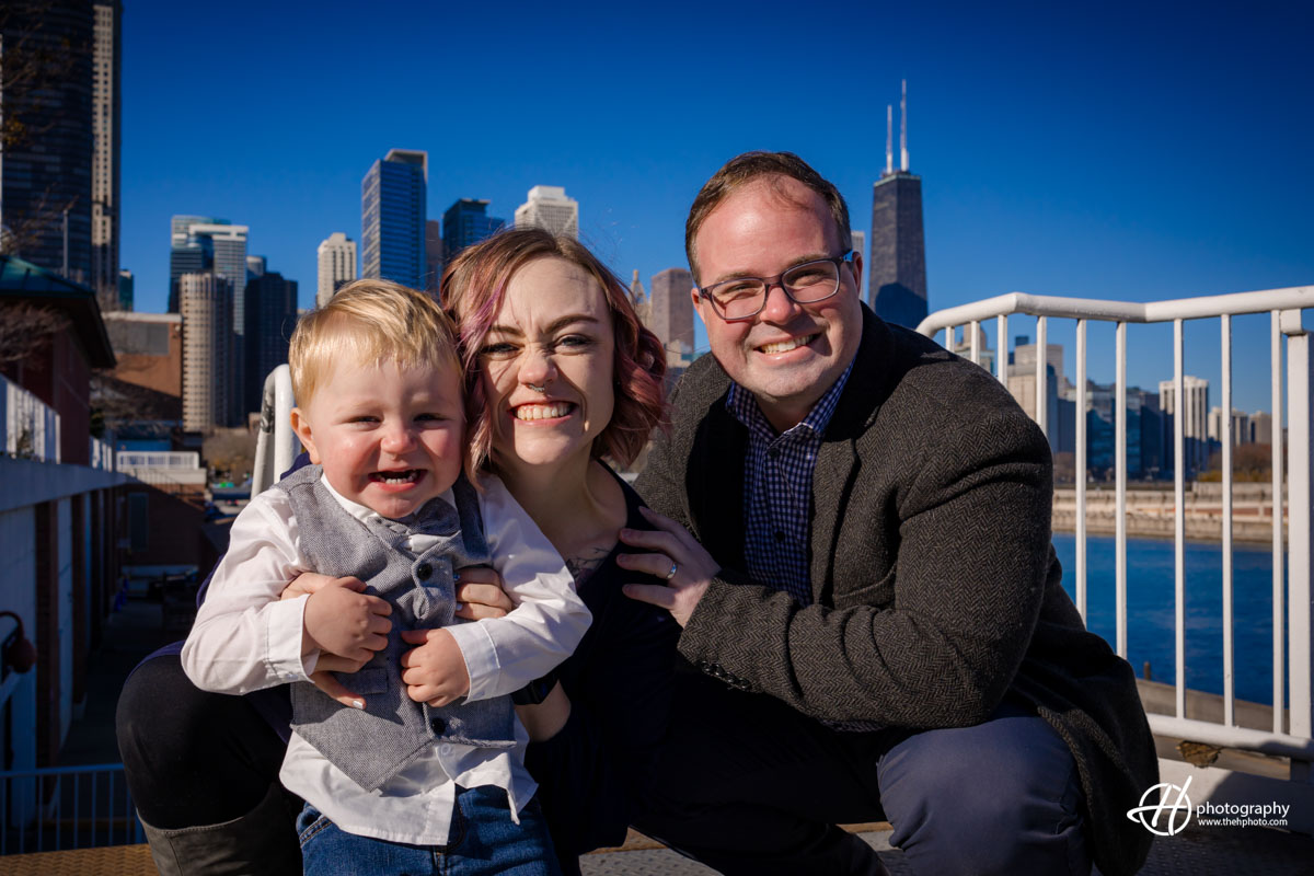 "Radiant family portrait: Sara, Todd, and their children stand against the backdrop of the iconic Hancock Tower in Chicago. The family exudes warmth and connection, framed by the cityscape that includes the towering presence of the Hancock Tower, creating a timeless and memorable image."