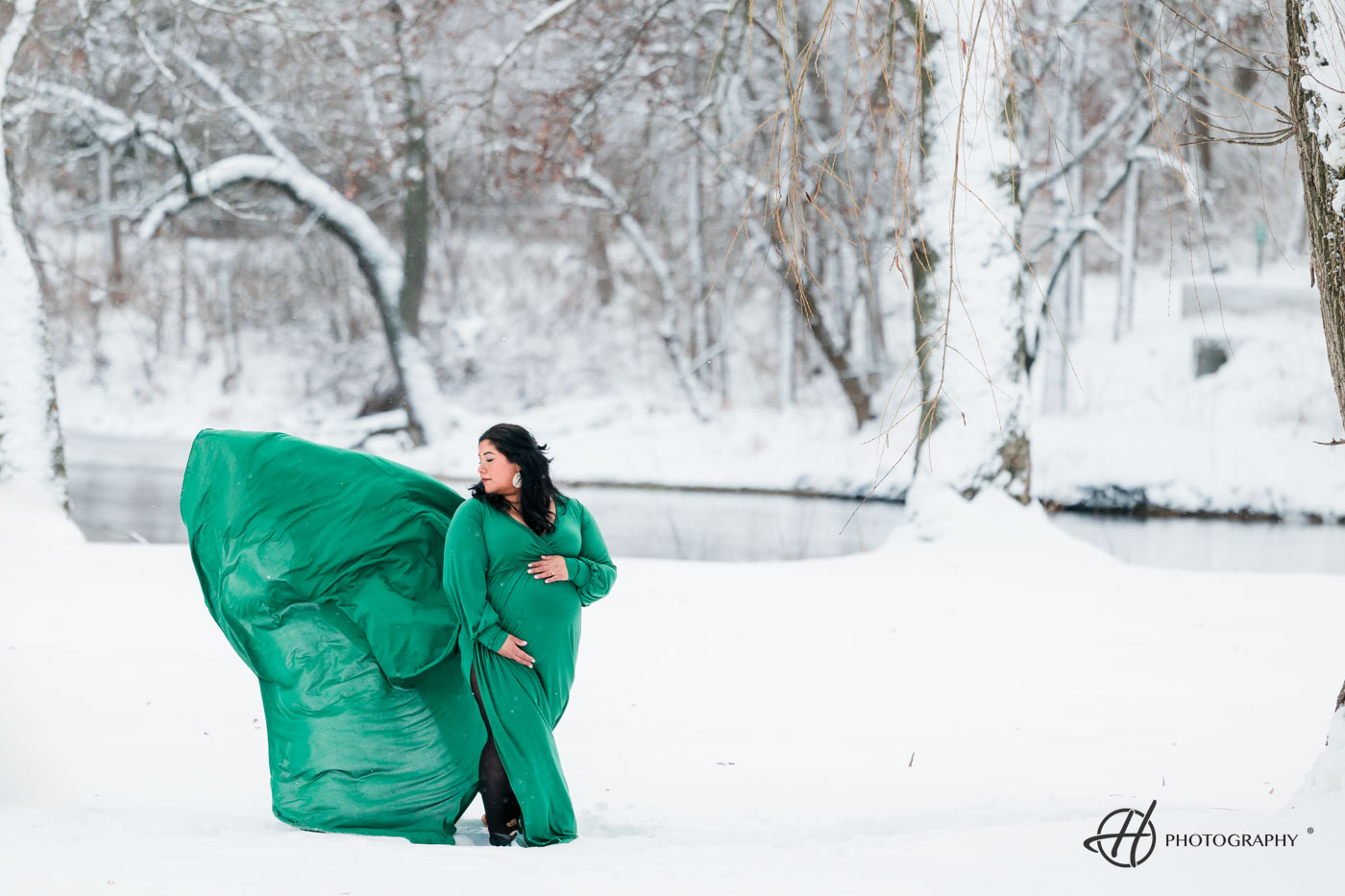 Pregnant woman in flowing green dress embraces the winter wind amidst a snowy landscape