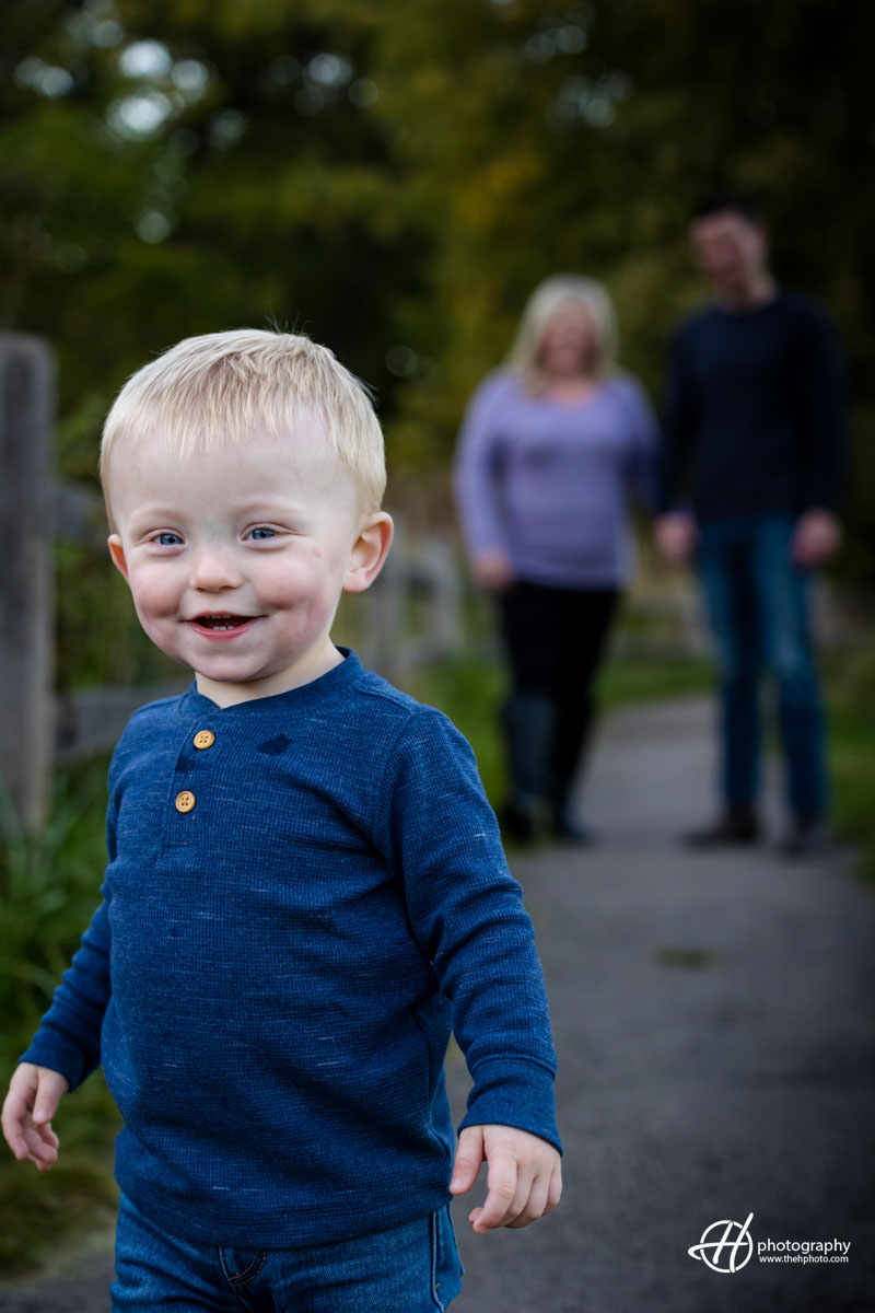 Eli smiling in foreground while parents watch him from the background 